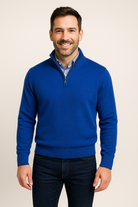Man wearing a blue sweater over a collared shirt on a beige background